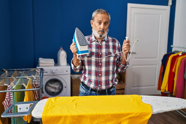 Rosnący starszy mężczyzna zmagający się z żelazną maszyną w pralni - portret sceptycznego, nerwowego i negatywnego charakteru zdenerwowanego problemami domowymi - Zdjęcie, obraz