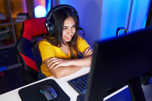 Jovem bela árabe mulher streamer sorrindo confiante sentado com braços cruzados gesto na sala de jogos - Foto, Imagem