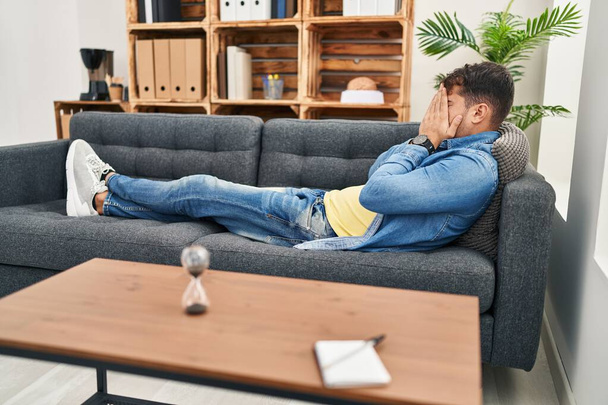 Young hispanic man patient stressed lying on sofa at psychology clinic - Foto, Imagem
