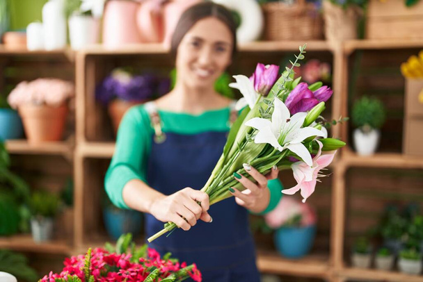 Young beautiful hispanic woman florist holding bouquet of flowers at flower shop - Fotografie, Obrázek