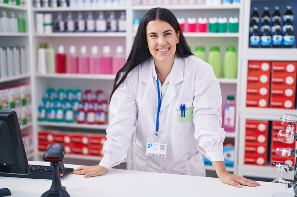 Joven hermosa mujer hispana farmacéutica sonriendo confiada de pie en la farmacia - Foto, Imagen