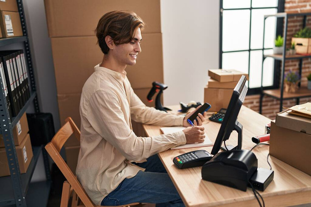 Joven hombre caucásico comercio electrónico trabajador de negocios utilizando la escritura de teléfonos inteligentes en el portátil en la oficina - Foto, Imagen