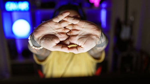 Un joven hispano con barba extiende los dedos en una oscura habitación interior iluminada por luces de neón. - Foto, imagen