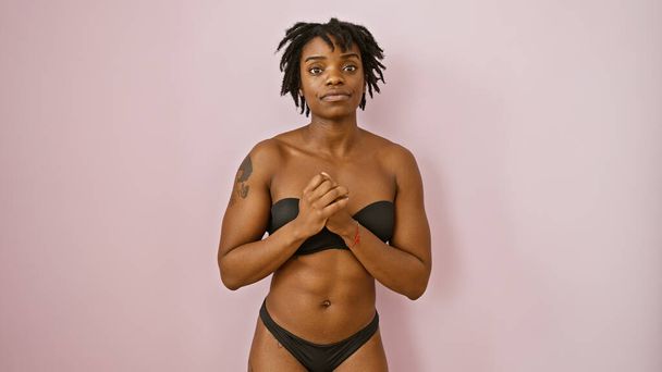 Eine selbstbewusste junge schwarze Frau mit Dreadlocks steht isoliert vor einer rosafarbenen Wand und porträtiert ein modernes Porträt. - Foto, Bild