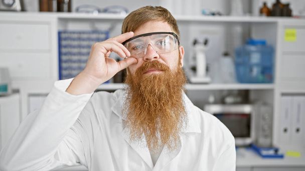 Uvolněný, ale vážný mladý rusovlasý vědec, umocněný průlomovým experimentem v laboratoři, zajišťuje bezpečnost s bezpečnostními brýlemi - Fotografie, Obrázek