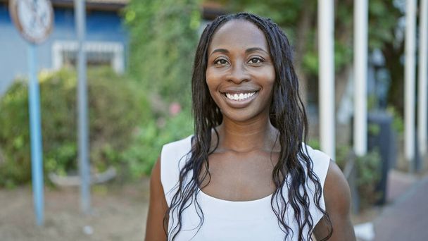 Portrait d'une jeune femme afro-américaine souriante aux cheveux bouclés, en plein air dans un cadre urbain. - Photo, image