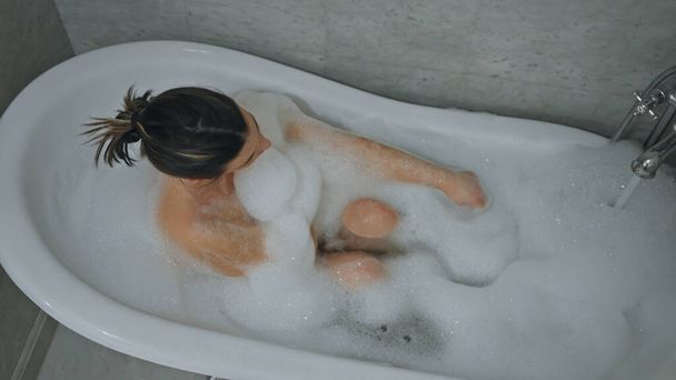 Horní pohled na mladou ženu, která odpočívá sama v pěnové vaně uvnitř, zobrazuje wellness a self-care. - Fotografie, Obrázek