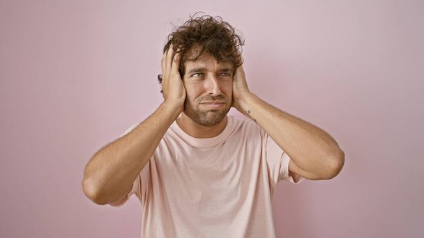 Egy problémás spanyol fiatalember rózsaszín ingben áll egy rózsaszín falnak támaszkodva, frusztráltan, kezekkel a fején.. - Fotó, kép
