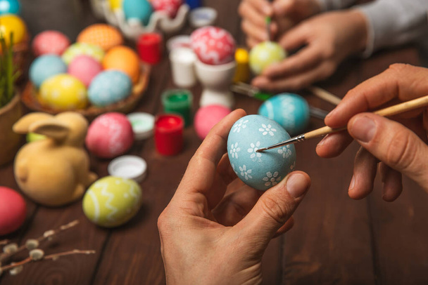 Hombre pinta huevos de Pascua en la mesa de madera de la cocina.Feliz Pascua celebración concept.Colorful huevos de Pascua con diferentes patterns.Paints, decoraciones para colorear huevos para holiday.Creative fondo. - Foto, imagen