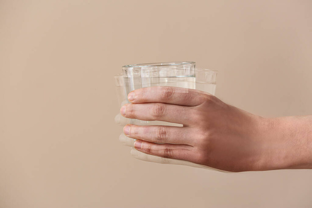 Дрожащая рука со стаканом воды на бежевом фоне. Месяц осведомленности Паркинсона - Фото, изображение