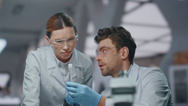 先進の実験室で医療プロジェクトを開発しているチーム生物学者. 重要な女性の同僚に医薬品サンプルを示す男性研究者. ワクチンの実験について話し合う2人の科学者. - 写真・画像