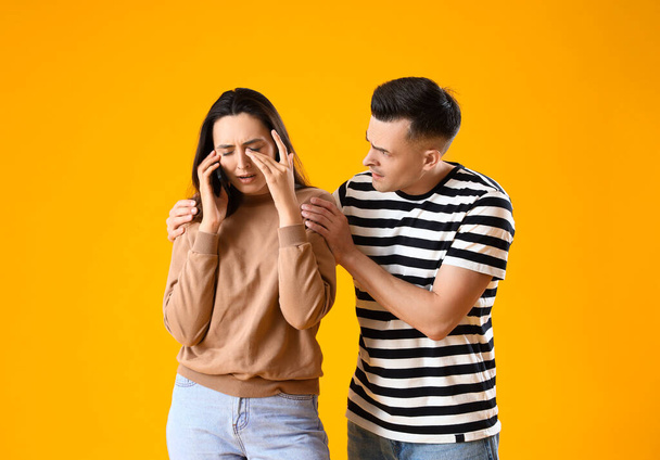 Расстроенная молодая женщина разговаривает по мобильному телефону и ее муж на желтом фоне - Фото, изображение