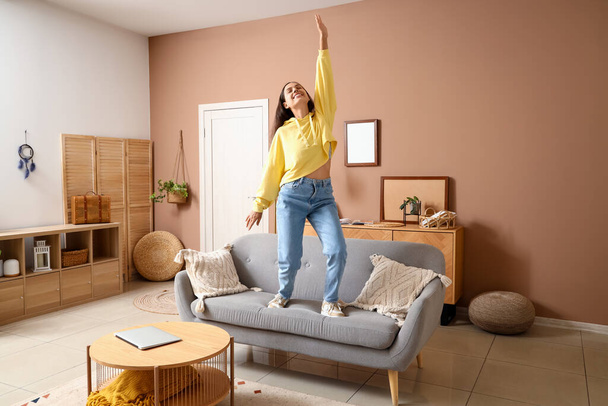 Mujer joven en sudadera con capucha bailando en el sofá en casa - Foto, Imagen