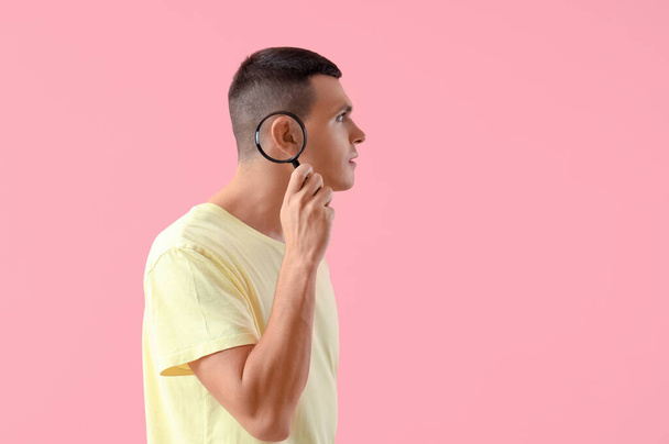 Młody człowiek z problemami ze słuchem i lupą na różowym tle - Zdjęcie, obraz
