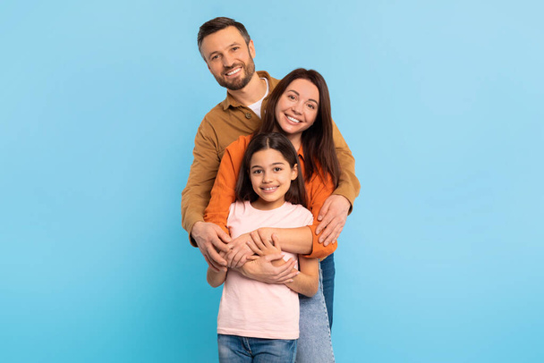 ハッピーな両親と子供の娘は,青い背景に対して強い家族の絆を示しています. 元気な父親,母親,子供の少女のスタジオポートレート - 写真・画像