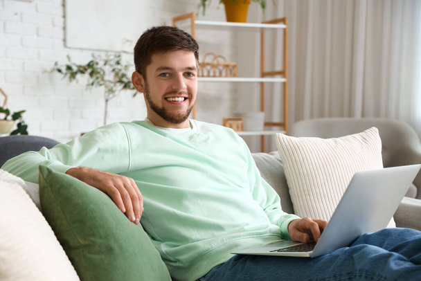 自宅でソファーでラップトップを使用するヤングひげ男 - 写真・画像