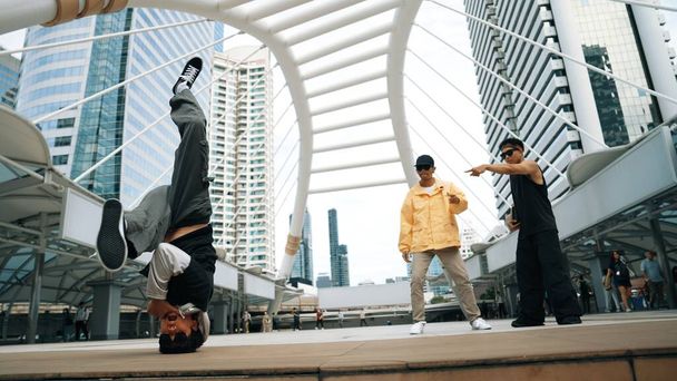 Grupa profesjonalnych ulicznych tancerzy rozchmurza się, podczas gdy azjatycki hipster wykonuje freestyle footstep w mieście otoczony przez ludzi z kamerą pod niskim kątem. Koncepcja break dance. Sport na świeżym powietrzu 2024. Sprytnie. - Zdjęcie, obraz