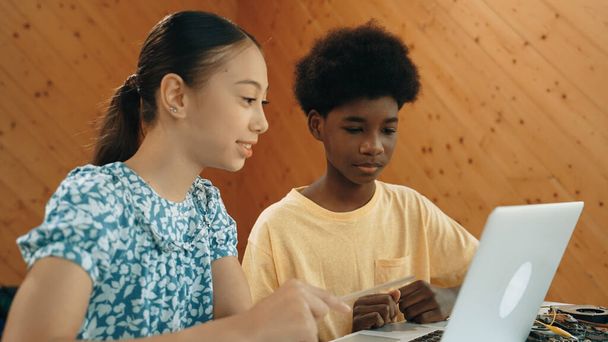 Afrika 'lı bir erkek ve beyaz bir kızın günlük giysiler içinde BTMM teknoloji sınıfında dizüstü bilgisayar ve elektronik ekipmanlarla kod yazma ya da programlama sisteminde birlikte çalıştıklarını gösteren site görüntüsü. Öğretim. - Fotoğraf, Görsel