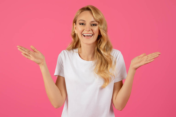 Wow aanbod. Portret van vrolijke jonge blonde dame in wit T-shirt reageren op geweldig nieuws, Handen in de buurt van gezicht terwijl glimlachen om de camera over Pink Studio achtergrond. Concept van opwinding - Foto, afbeelding