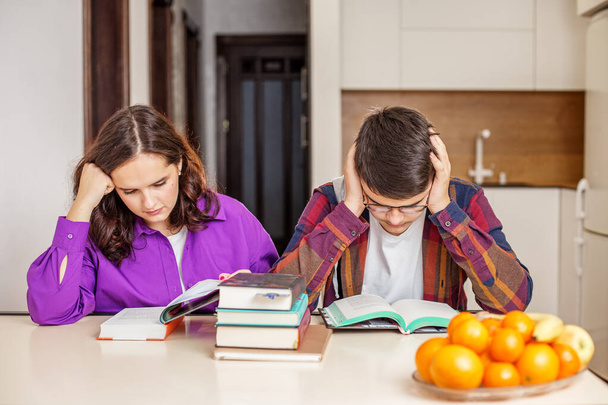 Δύο έφηβοι αφοσιωμένοι στη μελέτη με ένα σωρό βιβλία, επιδεικνύοντας ένταση της προετοιμασίας για τις σχολικές εξετάσεις στο σπίτι.. - Φωτογραφία, εικόνα