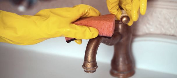 Una mujer con guantes de goma está limpiando la casa, creando limpieza y desinfección, limpiando el grifo y lavando el lavabo en el baño con una esponja. - Foto, imagen