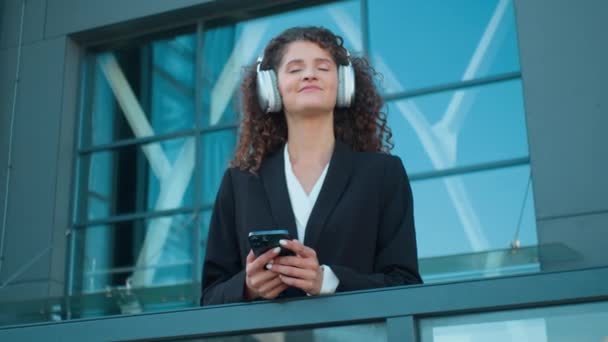 Heureux satisfait femme d'affaires caucasienne écouter de la musique dans les écouteurs sur la terrasse de la ville détendu souriant femme d'affaires entrepreneur employé de bureau prendre une pause de travail écouter chanson préférée se détendre à l'extérieur - Séquence, vidéo