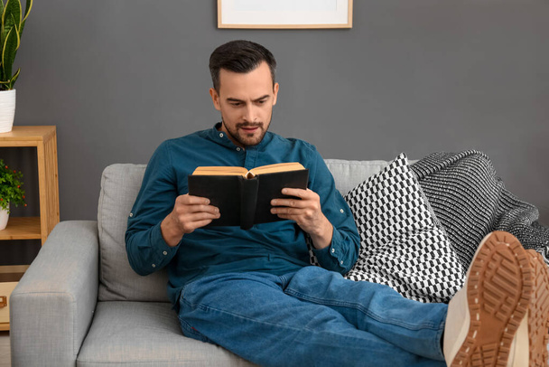 Handsome man reading book on sofa at home - Photo, Image