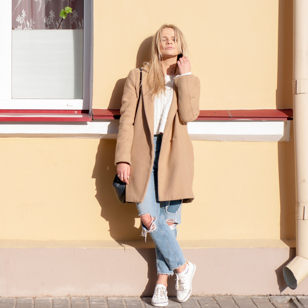 Young pretty fashionable blonde woman dressed in ripped jeans and beige coat - Foto, immagini