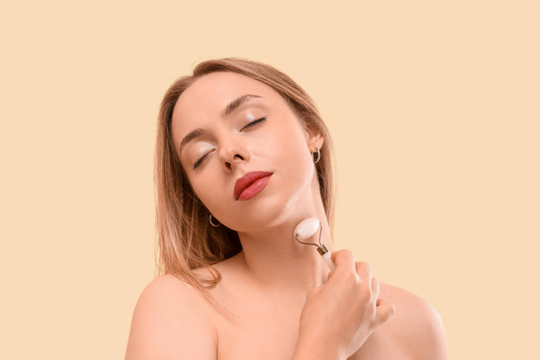 Młoda kobieta za pomocą wałka do masażu twarzy na beżowym tle - Zdjęcie, obraz