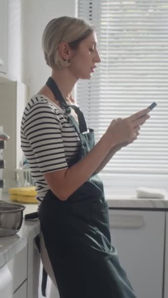 Tiro vertical de la mujer que pide comestibles en línea utilizando el teléfono móvil en casa - Imágenes, Vídeo