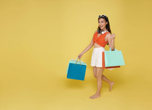Portret glimlachen aantrekkelijk aziatische vrouw in de zomer jurk holding shopping tas zomer verkoop geïsoleerd op gele achtergrond. - Foto, afbeelding