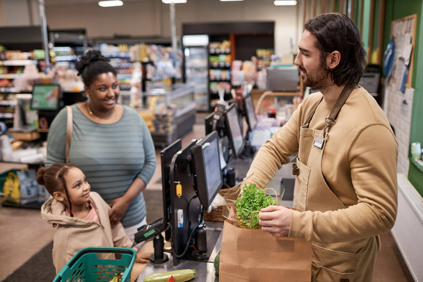 Seitenansicht Porträt eines lächelnden männlichen Arbeiters im Supermarkt, der jungen Frau beim Einkaufen hilft - Foto, Bild