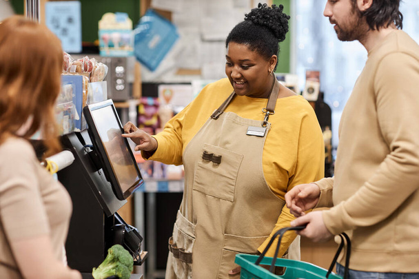 Portrait à la taille d'une femme noire souriante aidant les clients avec l'auto-paiement dans un supermarché - Photo, image