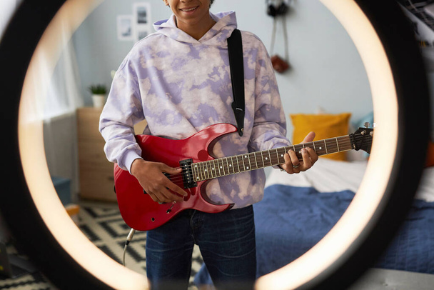 Обрізаний знімок щасливого хлопця-підлітка з електрогітарою, що стоїть за круглою рамкою для відеозйомки та гри на музичному інструменті - Фото, зображення