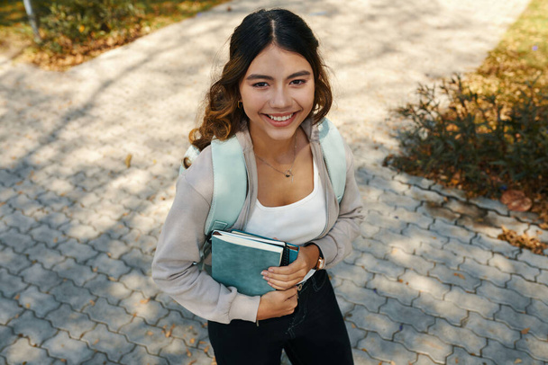 Portrait of cheerful schoolgirl holding books and looking up at camera - Photo, Image