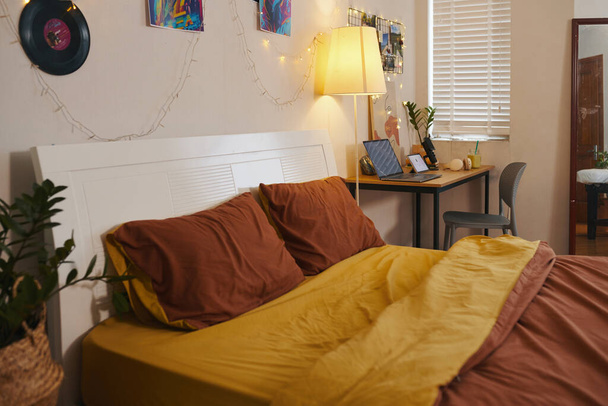 Bequemes Bett und Schreibtisch mit offenem Laptop im Schlafzimmer eines Teenagers - Foto, Bild