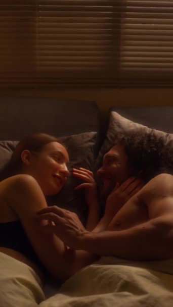 Yatakta uzanan, birbirlerini okşayan ve romantik sohbetler eden genç çiftlerin dik açılı görüntüsü. - Video, Çekim