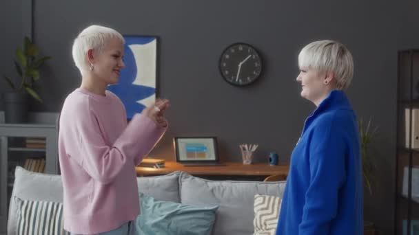 Foto media de dos jóvenes amigas caucásicas que se comunican con el lenguaje de los dedos de las señas de pie en un apartamento moderno durante el día - Metraje, vídeo