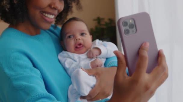Kézi felvétel fiatal gyönyörű afro-amerikai nő csinál szelfi portré okostelefon egy hónapos baba fia otthon - Felvétel, videó
