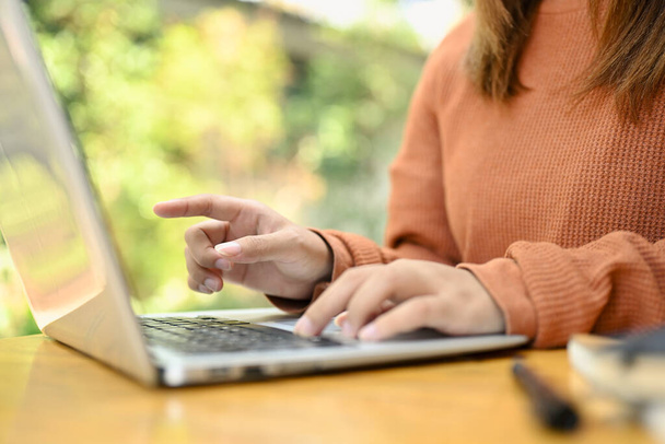 Femme pigiste en pull marron tapant sur ordinateur portable, cherchant des informations ou travaillant en ligne. - Photo, image