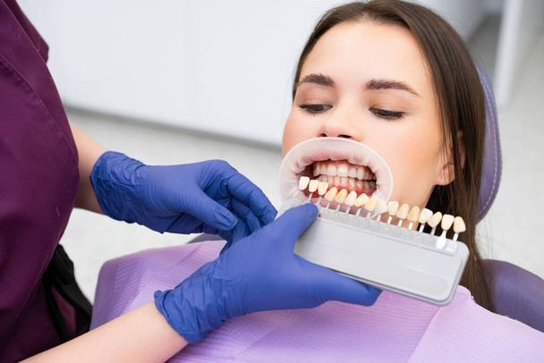Стоматолог вибирає відтінок відбілювання зубів за допомогою керівництва відтінками для молодої жінки з ідеальною посмішкою - Фото, зображення