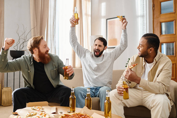 Tres hombres guapos de diferentes razas se sientan en un sofá, disfrutando de la cerveza y la pizza en un ambiente acogedor. - Foto, Imagen