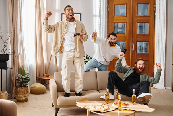 Drei fröhliche, gut aussehende Männer verschiedener Rassen entspannen sich in einem gemütlichen Wohnzimmer, genießen die Gesellschaft des anderen und bauen Freundschaft auf. - Foto, Bild