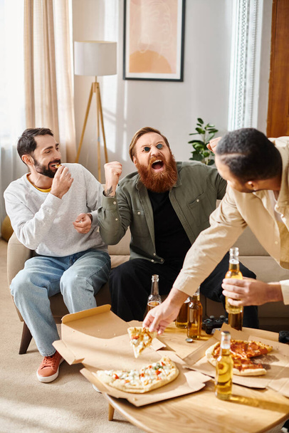 Drei gut gelaunte, gutaussehende Männer unterschiedlicher Rassen genießen an einem Tisch in gemütlicher häuslicher Umgebung Pizza.. - Foto, Bild