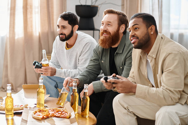 Trzech wesołych, przystojnych, międzyrasowych mężczyzn w luźnych strojach siedzi przy stole, dzieląc się piwem i pizzą, ciesząc się swoim towarzystwem.. - Zdjęcie, obraz
