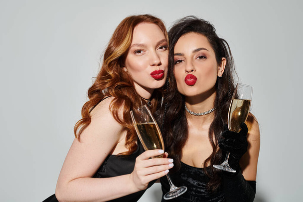 Una pareja lesbiana cariñosa con un atuendo elegante, felizmente sosteniendo copas de vino. - Foto, Imagen