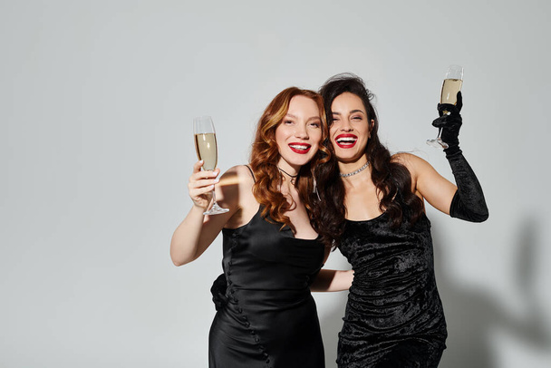 Дві елегантні жінки в чорних сукнях радісно тост з флейтами шампанського. - Фото, зображення