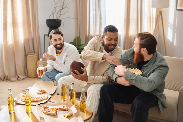 Tres hombres elegantes y diversos comparten alegremente pizza y cerveza en un acogedor sofá en casa. - Foto, imagen