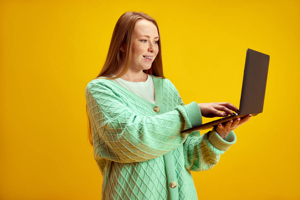 Portrait of young attractive woman wearing casual clothes with red hair looking at tablet against yellow studio background. Concept of online working, shopping, freelance, delivery, technology. Ad - Photo, Image