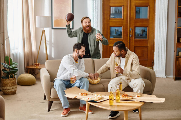 Tres hombres alegres y guapos de diferentes razas disfrutando de la compañía de los demás en la parte superior de un sofá mientras se visten casualmente en casa. - Foto, imagen